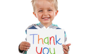 Child holding a crayon thank you sign standing against white background