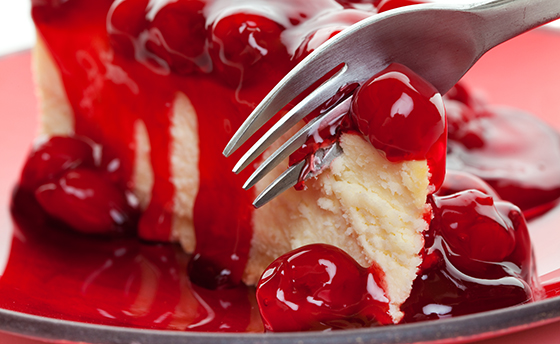 A fork slicing into a piece of cherry cheese cake