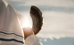 Jewish man blowing the Shofar with hebrew words from the prayer book in the background