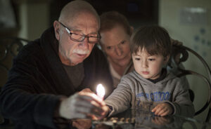 Jewish Family with granparents and grandson lighting Hanukkah Candles in a menorah for the holidays