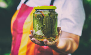 Senior woman holding a jar of pickles in the garden. Homemade pickled cucumbers in a glass jar.